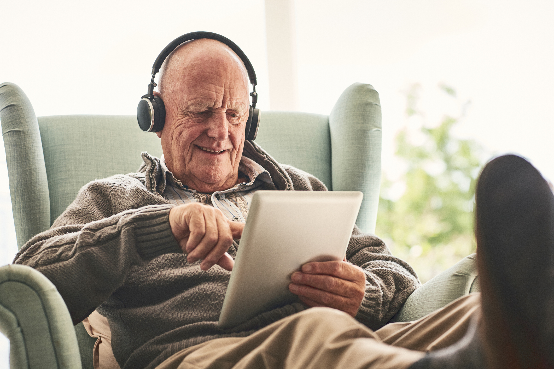 older adult sitting using iPad with headphones on