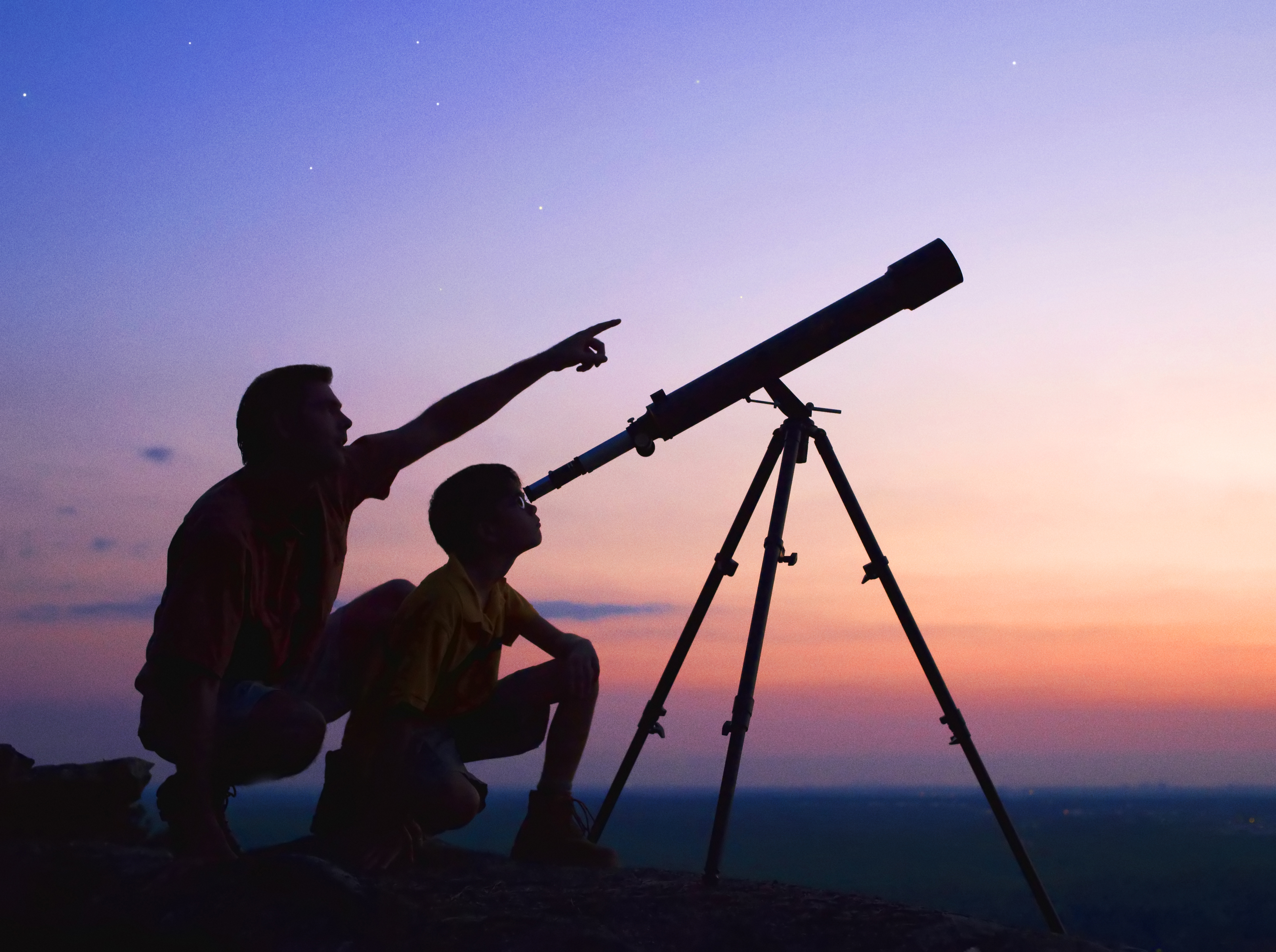 Two people looking at the night sky through a telescope.