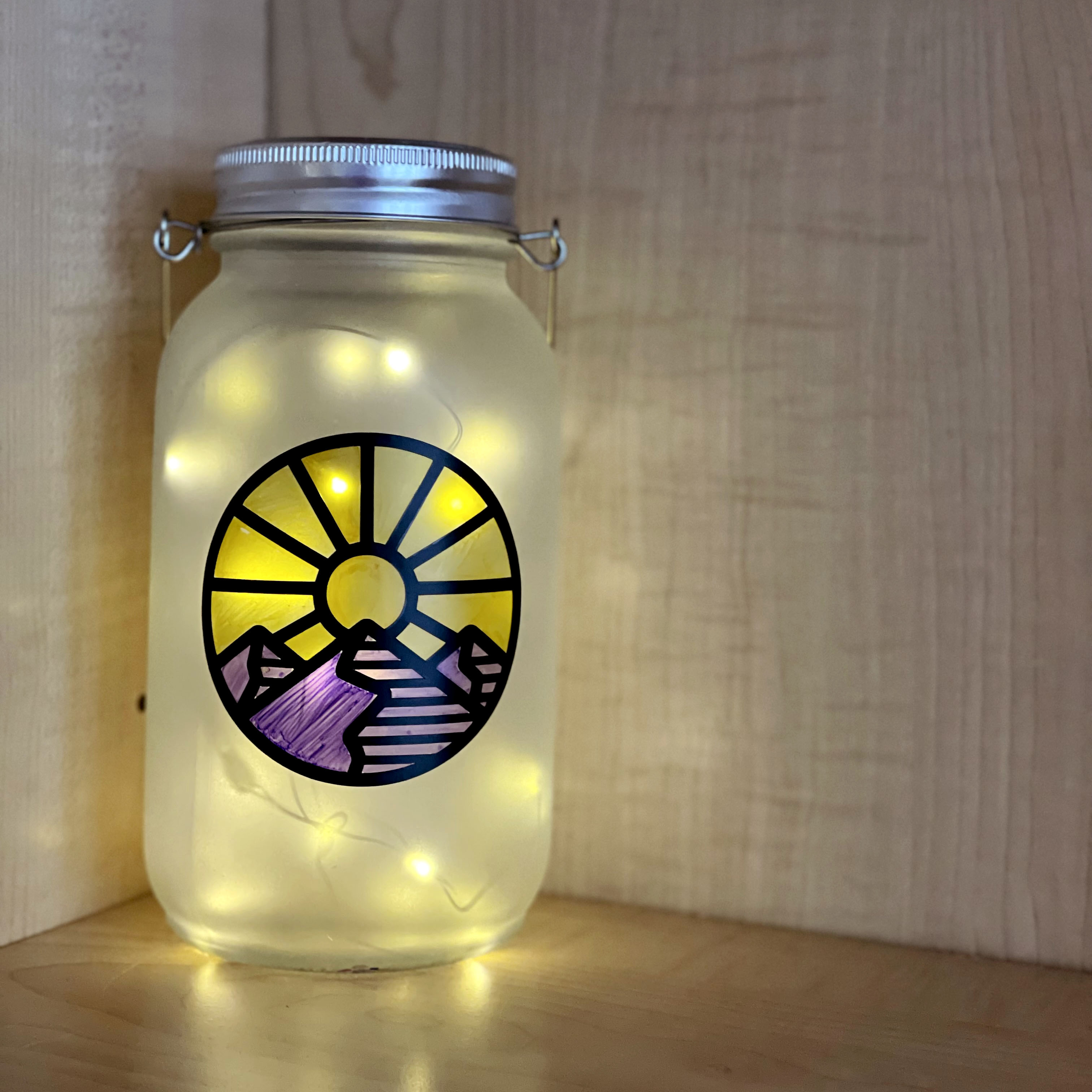 Glowing frosted mason jar with vinyl mountain sunset scene colored in with markers.