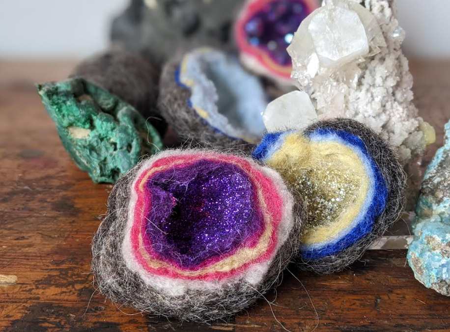 Colorful felted geodes with real geodes in the background on a brown table