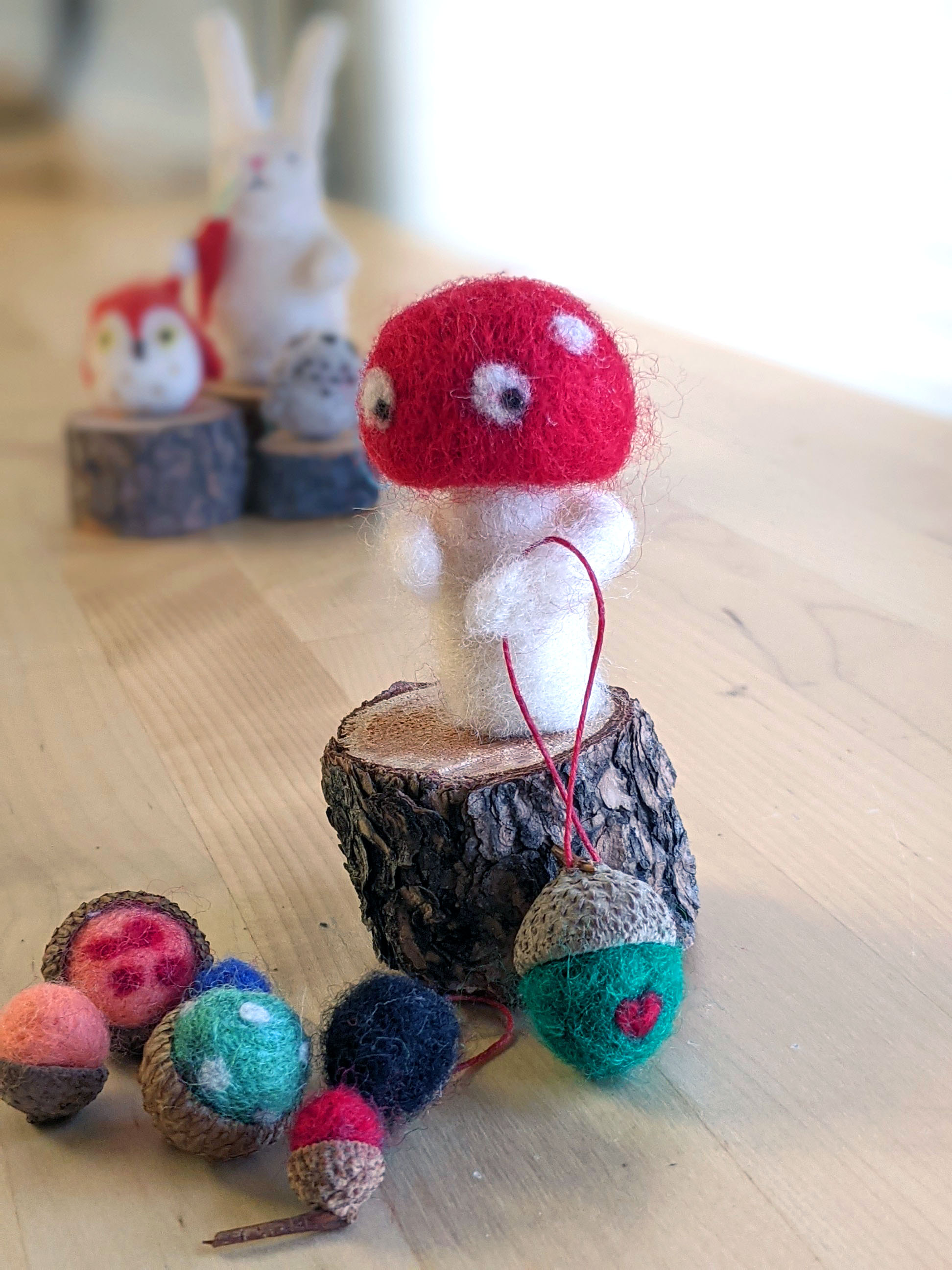 Needlefelting mushroom and acorns on a piece of wood with needlefelted bunny in the background