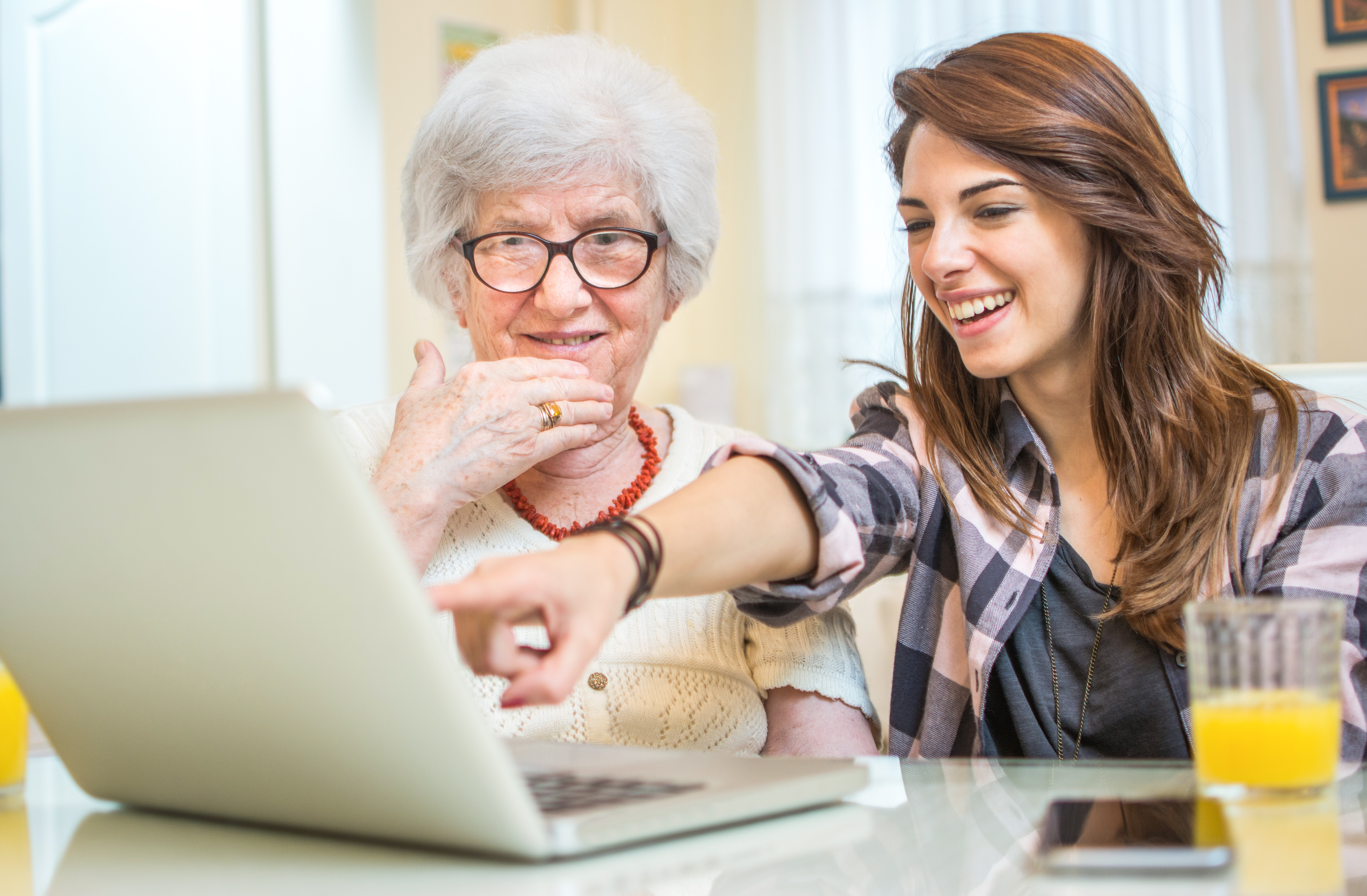 A young woman points at an open laptop to show an older woman something on the screen