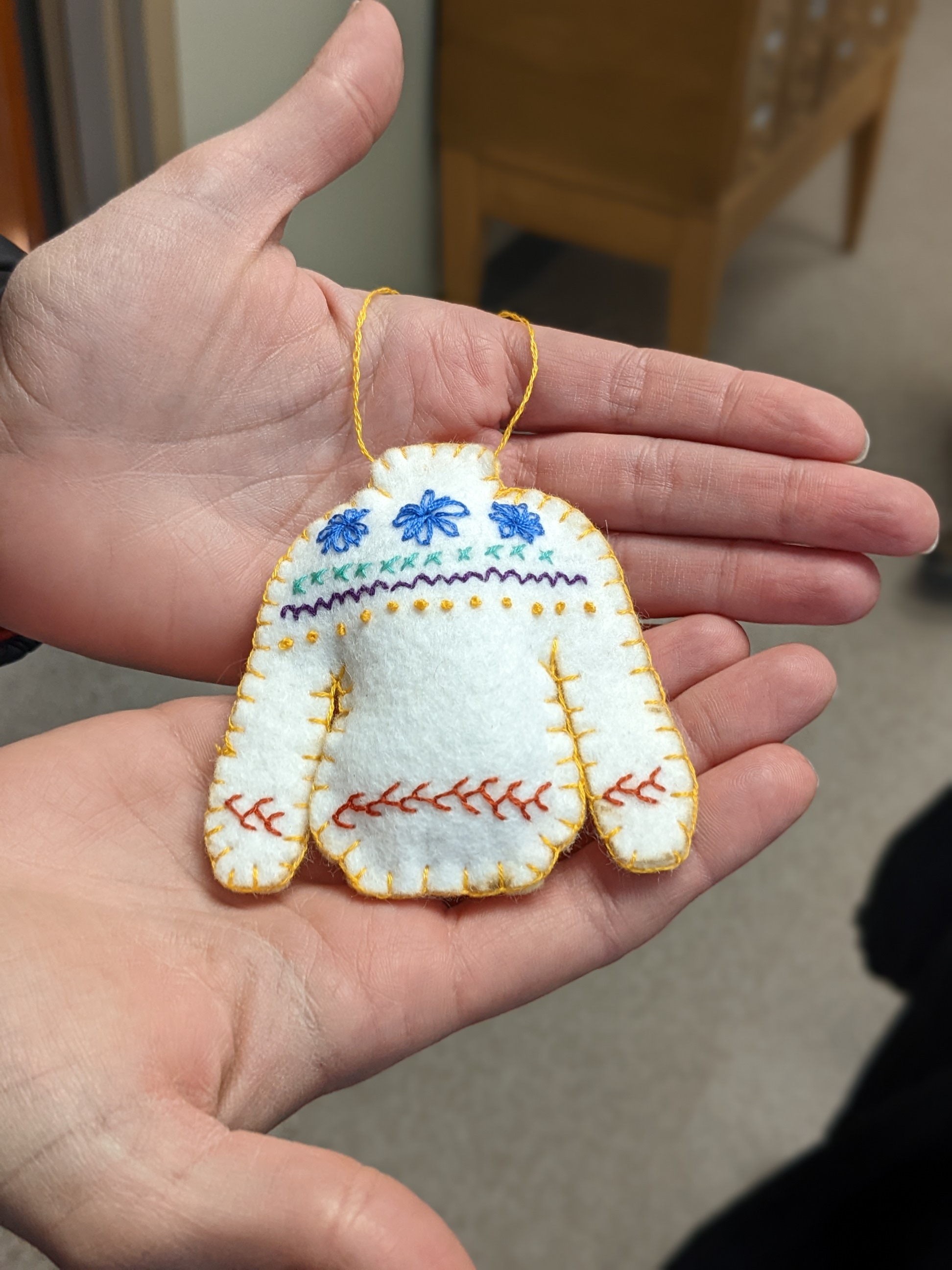 Two hands holding a hand-sewn and hand-embroidered felt ornament that looks like a sweater.