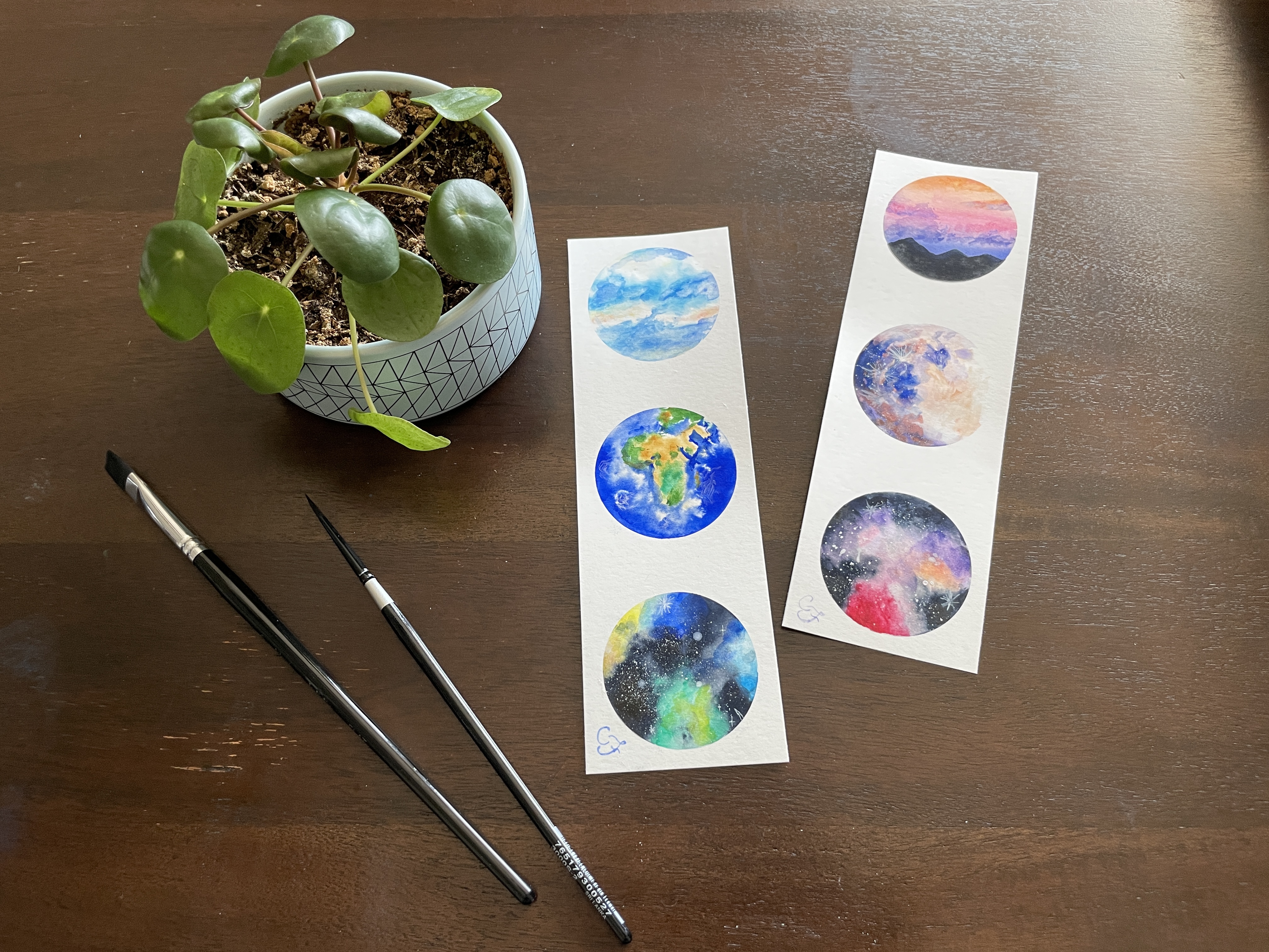 watercolor of space and nature on bookmarks alongside plant