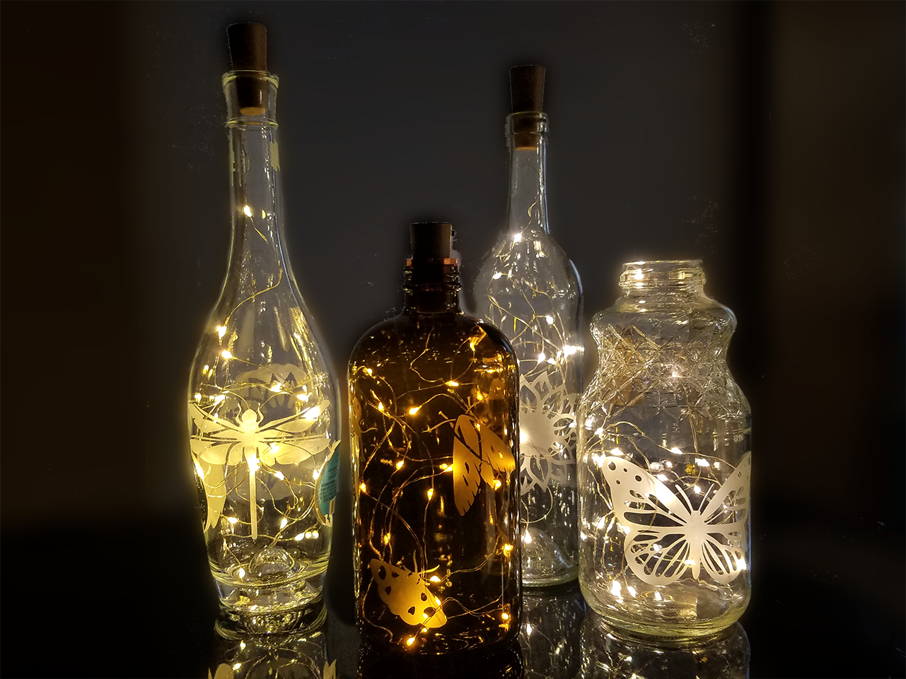 Bottles etched with insect and nature designs and glowing from string lights placed inside.