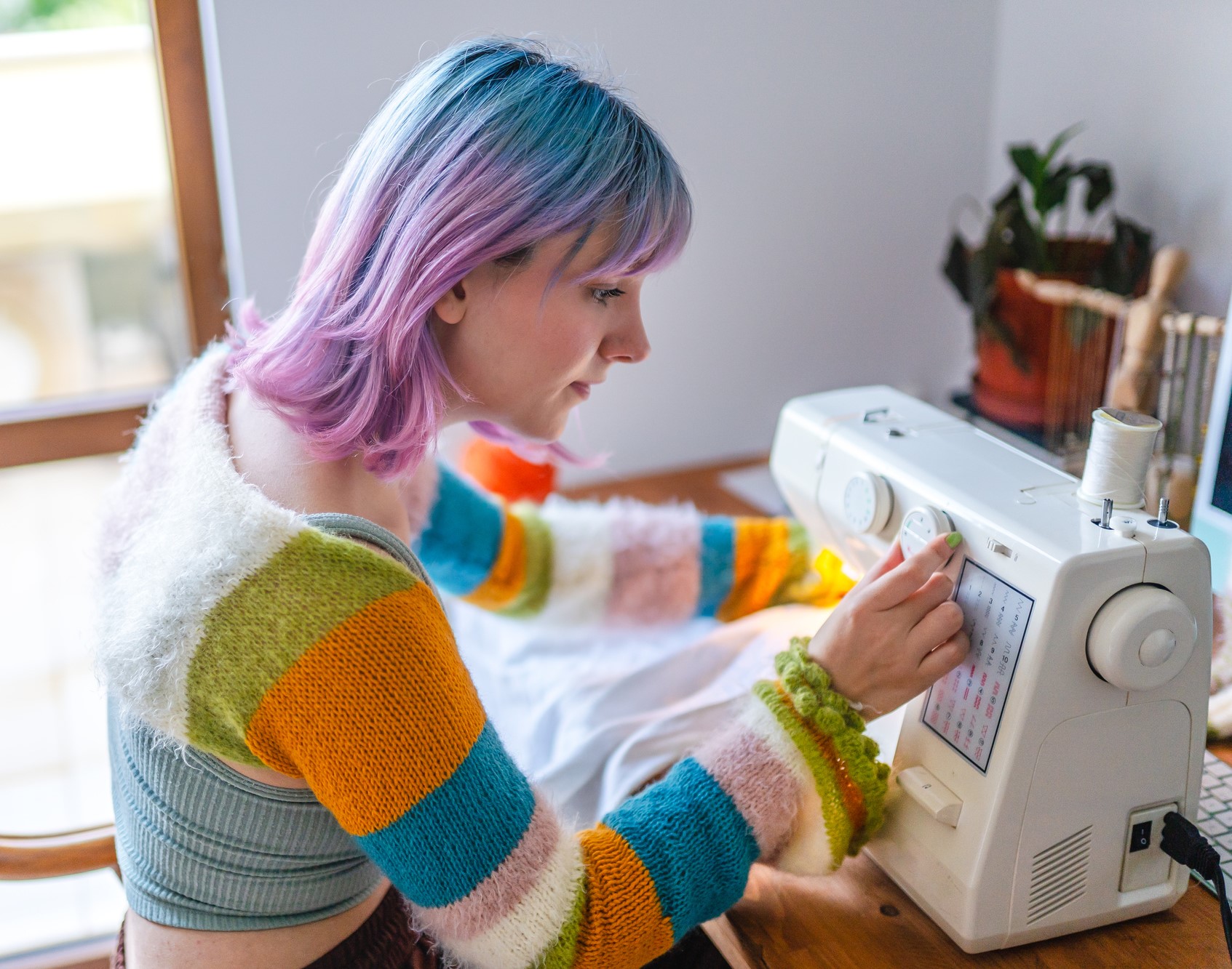 Person with blue and pink hair adjusting a dial on a sewing machine