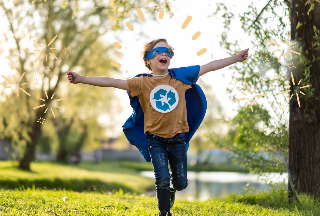 A child running with his arms stretched out into the air, across a patch of green grass with a few trees in the background. He is wearing a yellow shirt with a recycle symbol in the center, a blue cape, and a blue superhero mask. 