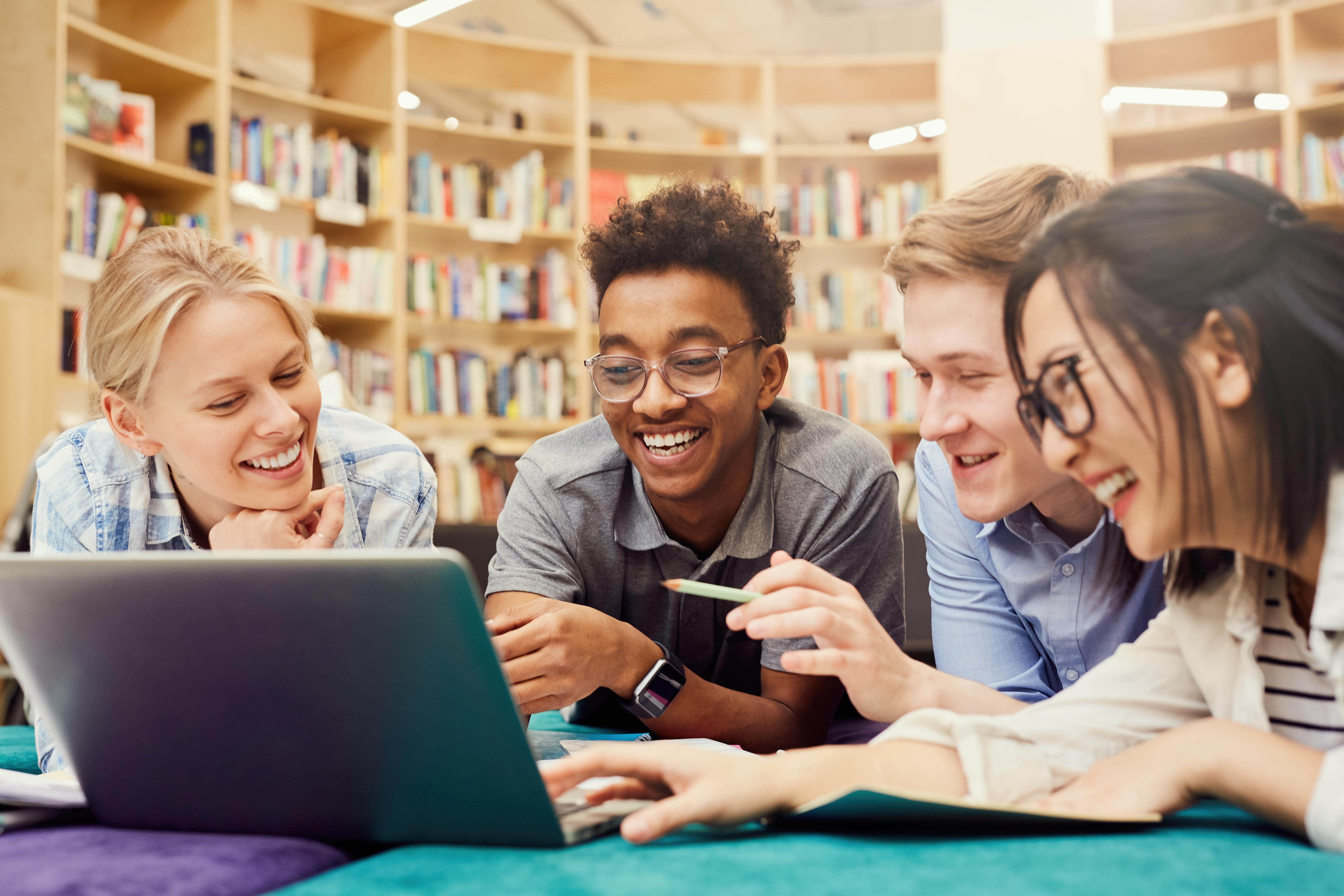 A diverse group of four teenagers sitting in a library looking at a computer together.