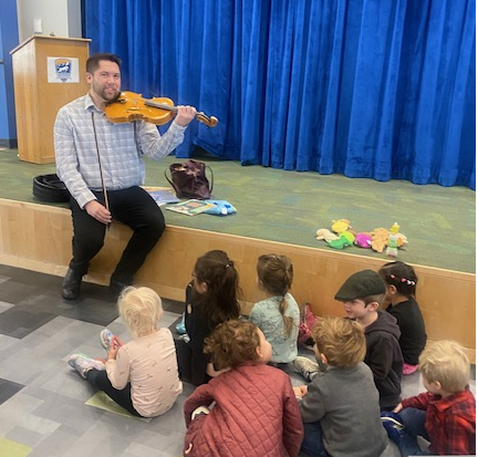 Adult playing stringed instrument for group of young children