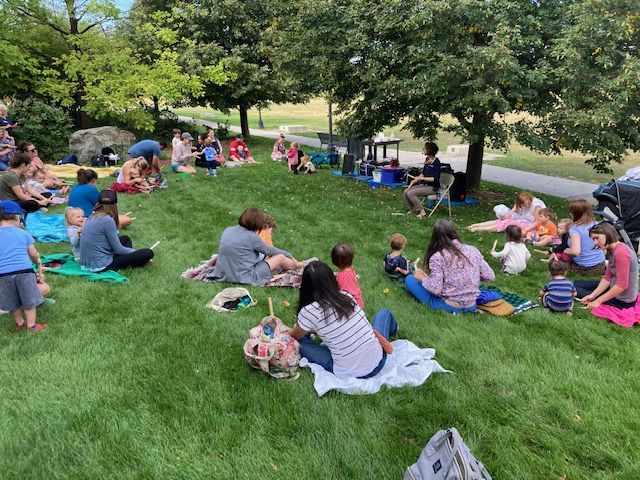 Outdoor storytime.  Families sitting on blankets in the grass.