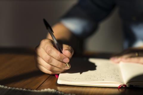 an adult male hand holding a pen over a journal he is writing in