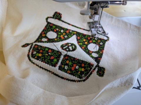 Flower pattern fabric cut in shape of a VW camper van that is being sewn onto white fabric..