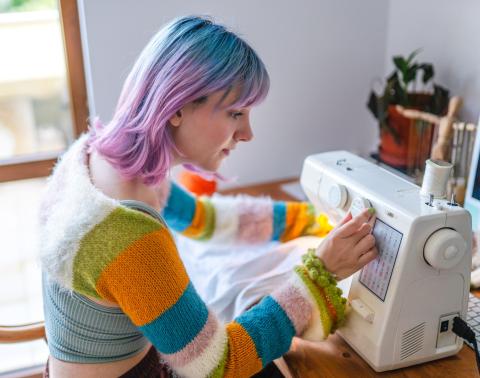 Person with blue and pink hair adjusting a dial on a sewing machine