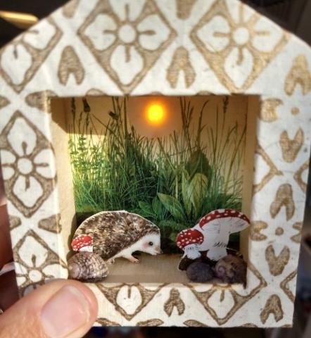 Illuminated sun above a hedgehog and mushroom scene in a box.