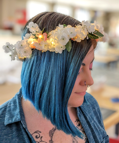 Close up of blue-haired woman posing with white flower crown headband glowing with fairy lights