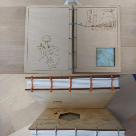 Wooden journal showing front and back covers with a laser etched drawing of a garden. Exposed spine shows coptic stitching. 