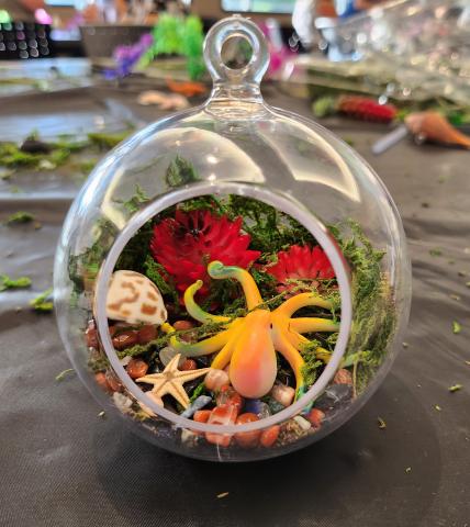 Plastic hanging terrarium with opening in front showcasing an octopus, sea shells, and other ocean themed decorations.