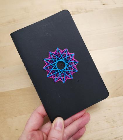 Hand holding a hand embroidered notebook with colorful geometric embroidery