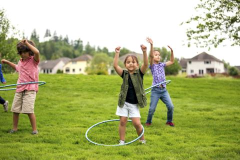 3 kids hula hooping on the grass.