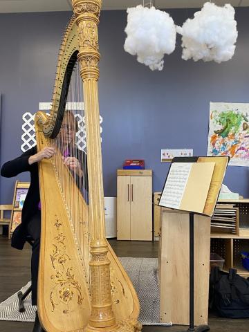 Woman playing a harp with a sheet of music on a stand.