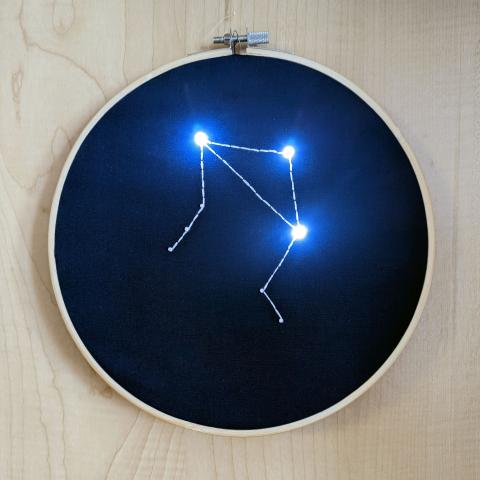 Hand embroidered constellation in an embroidery hoop with glowing LEDs for stars