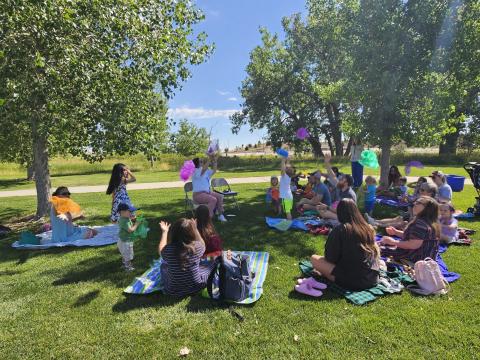 Kids throw scarves in the air as families sit on the grass in a park