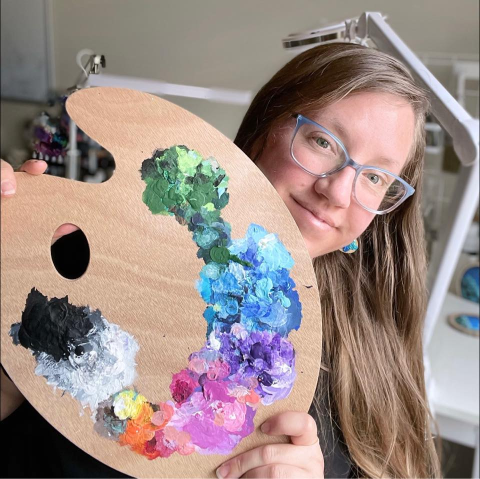 artist chrissy sparks holding an artist's palette with watercolor paints in a rainbow arc