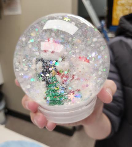 Hand holding a DIY snowglobe with white glitter swirling around a winter scene