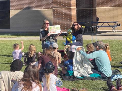 Librarians reading picture book outside with dragon puppet.