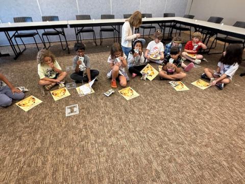Kids sitting in a circle reading and having snacks.