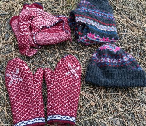 A pair of red mittens and matching hat next to a set of gray mittens and matching hat made of upcycled sweaters