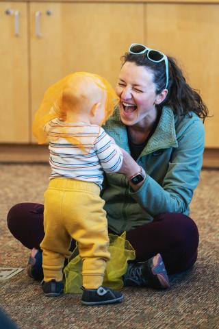 Caregiver and young child playing peek-a-boo with an orange scarf