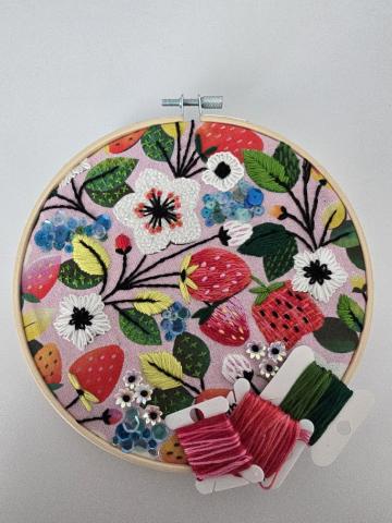 Embroidery in a hoop with stitches that form strawberries, flowers, and leaves
