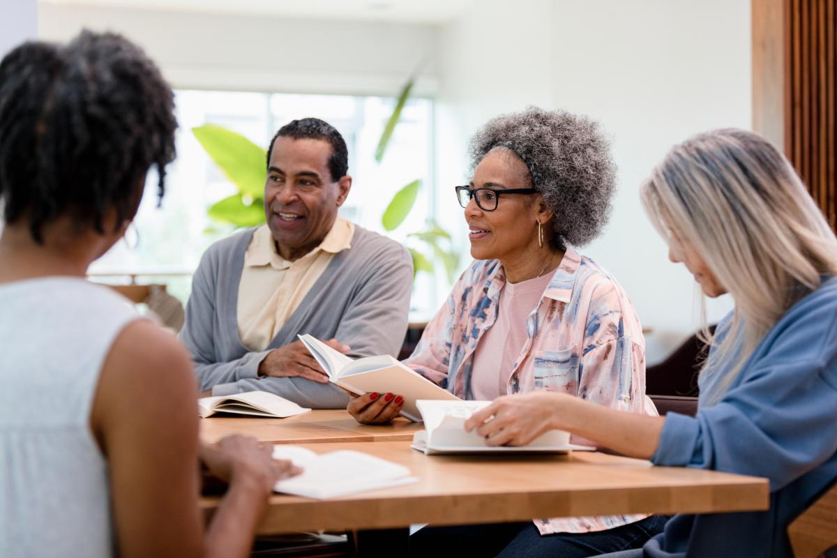 four adults sita round a table talking with books in their hands