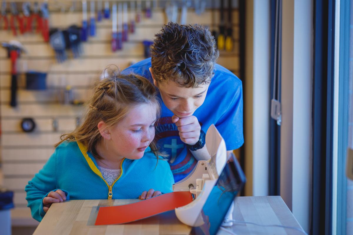 Two kids looking at a vinyl cutter working to cut out a vinyl sticker