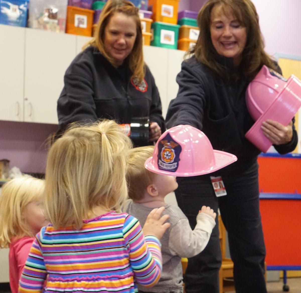 Two fire fighters handing out play helmets to kids in storytime