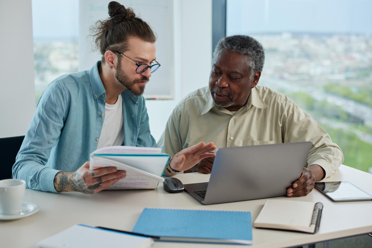 Photo of library staff assisting older adult patron on a laptop.