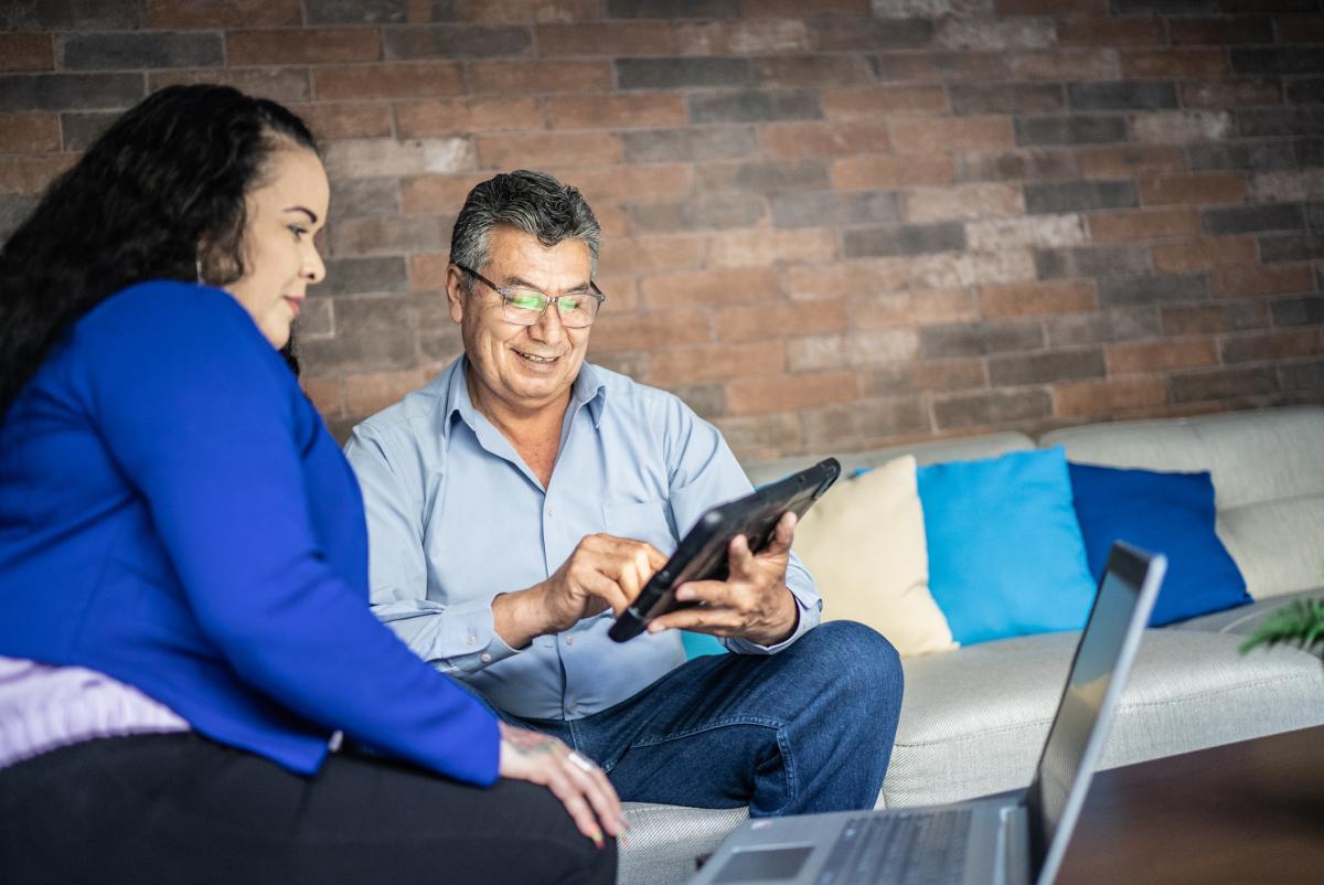 A woman and man looking at a mobile phone and laptop computer together.