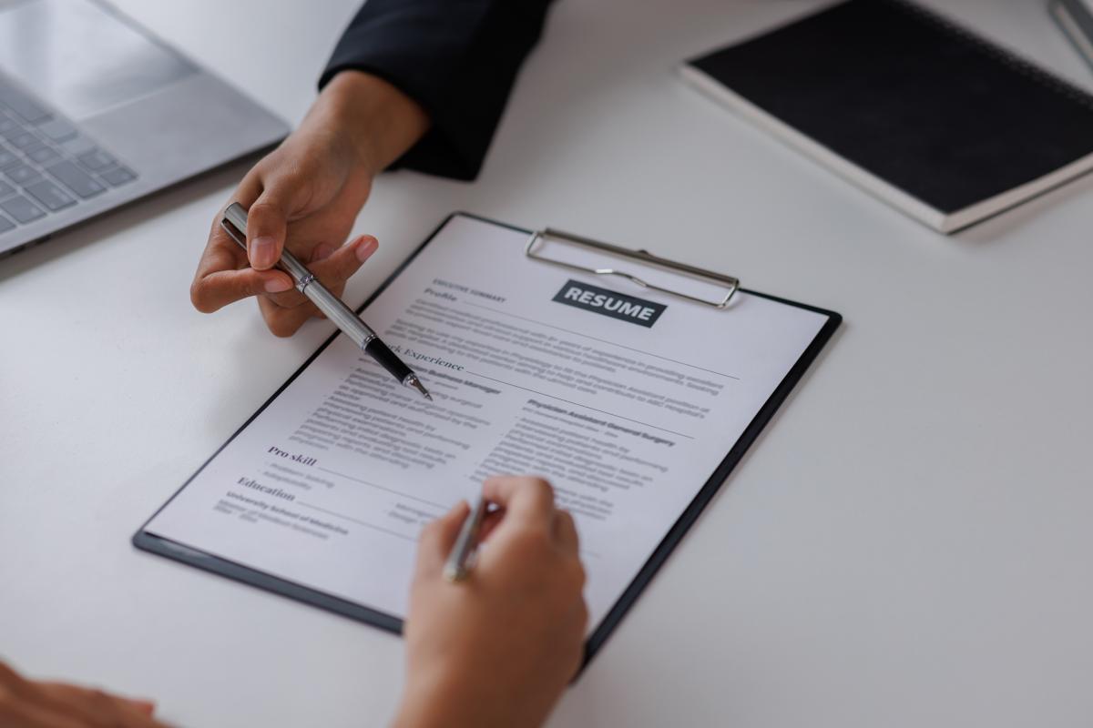 resume on a clipboard, two hands holding pens