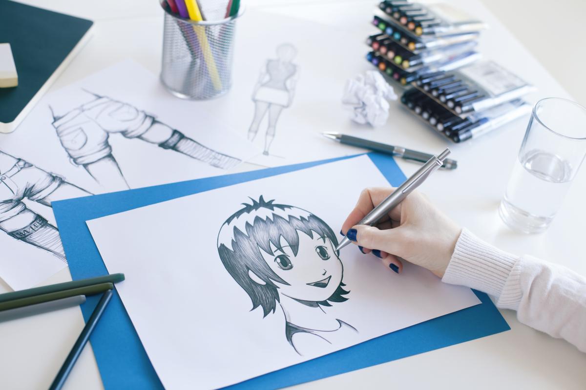 Desk with drawing materials, Manga style drawings and hand with blue fingernails.