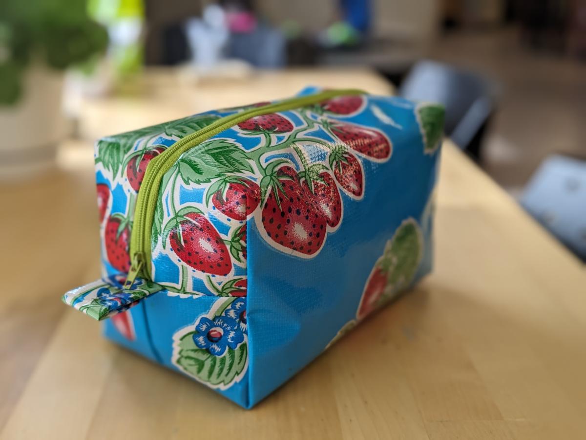 Dopp bag or toiletry bag made from oilcloth with a blue and strawberry pattern and red zipper.