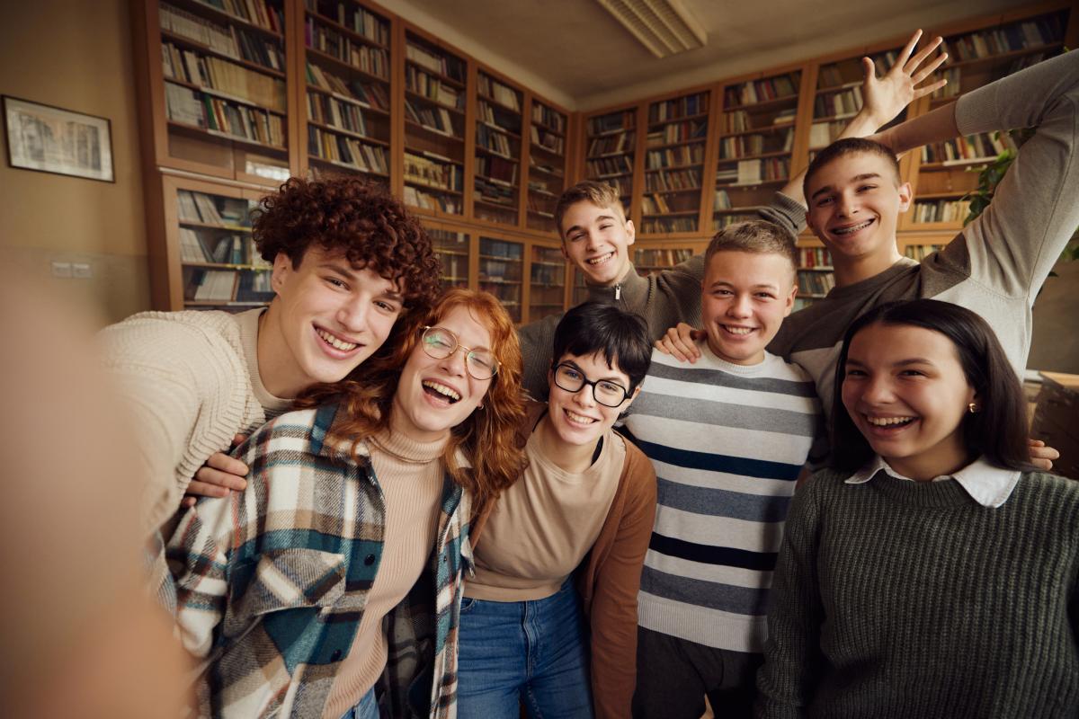 teens hanging out at the library with bookshelves in the background.