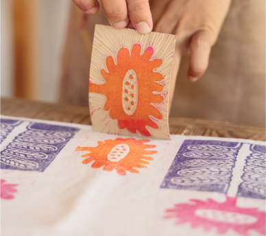 Hands holding a flower shaped stamp with orange ink used to print on fabric