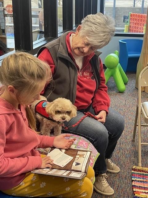 child reading to a dog with the dog handler.