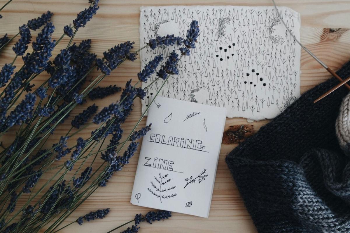 A zine titled "coloring zine" on a table with flowers and knitted garment