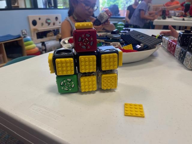 Cubelets stacked up with LEGO in the background on a table.