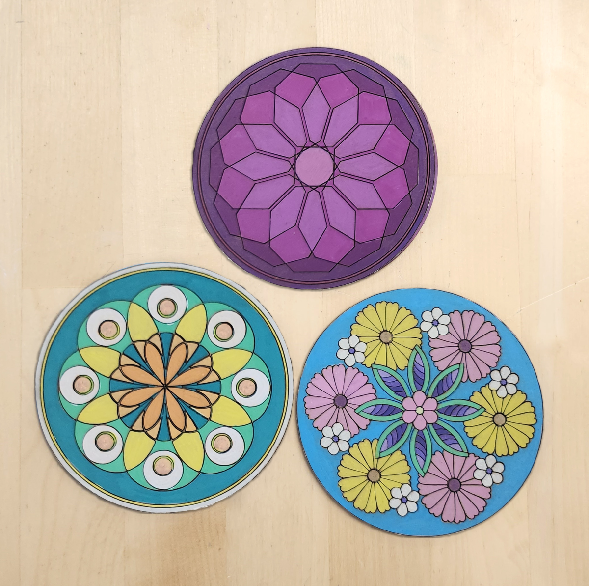 3 painted laser cut wood coasters decorated with colorful mandala patterns