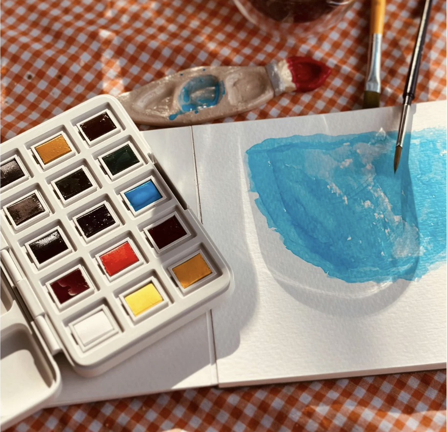 Watercolor paint palette on table with paintbrushes and paper
