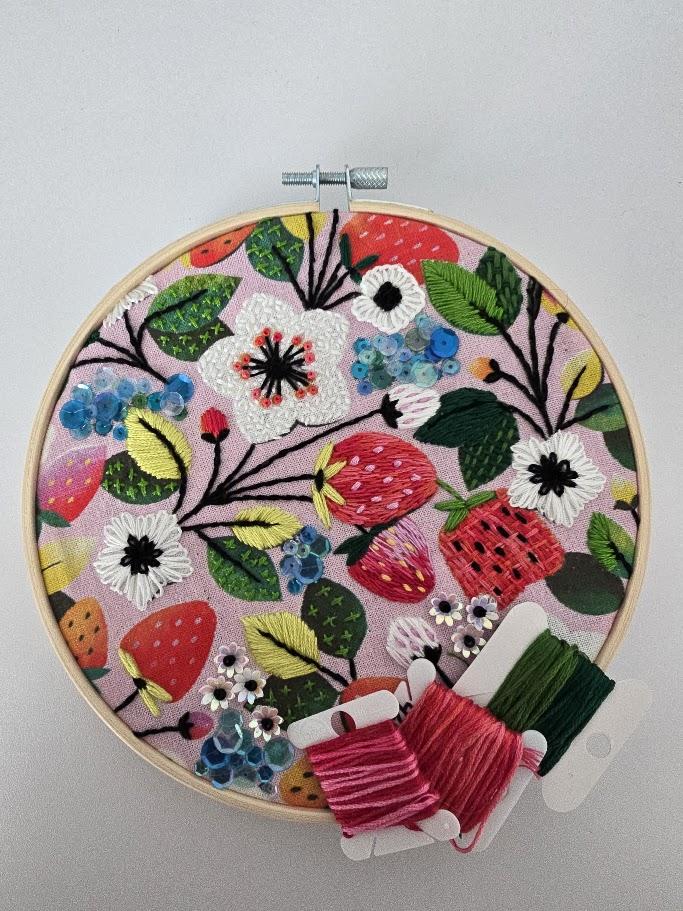 Embroidery in a hoop with stitches that form strawberries, flowers, and leaves